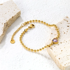 Dettaglio del bracciale a catena dorata con zircone a cuore viola e chiusura a moschettone
