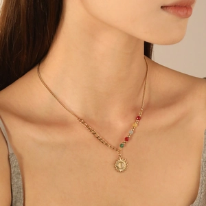 Close-up of a gold sun pendant necklace with colorful beads on an asymmetric chain