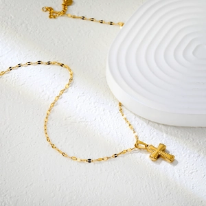 Detailed view of gold cross pendant with grainy border on fine water wave chain
