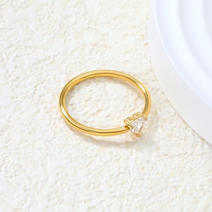 Macro detail of a minimalist gold ring featuring a heart-shaped zircon on a stone surface