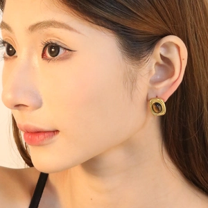 Ovale Tigerauge-Ohrringe mit goldenen Stahlkugeln an einem weiblichen Model für Eleganz