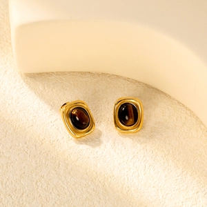 Detail von goldenen Vintage-Ohrringen mit Tigerauge-Stein auf texturiertem Grund