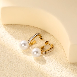 Detail of elegant gold-plated pearl earrings with inlaid crystals on a neutral base