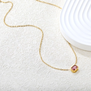 Detalle de colgante de gema rosa rectangular en collar de oro sobre mármol blanco puro