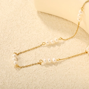 Macro detail of 18K gold-plated chain with small white pearls on textured background