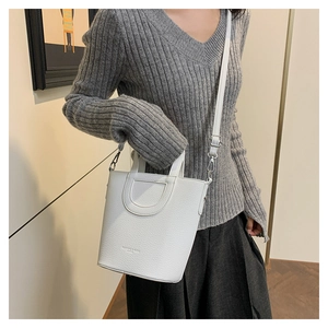 Macro detail of white lychee pattern leather bucket bag with embossed logo and fine stitching
