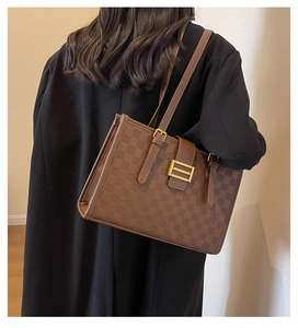 Detail of dark brown checkered tote bag with golden buckle on female model in black coat