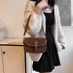 Vintage brown leather underarm bag with metal buckle strap shown in a minimalist room