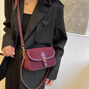Vintage burgundy suede crossbody bag with gold buckle on a model in a black blazer