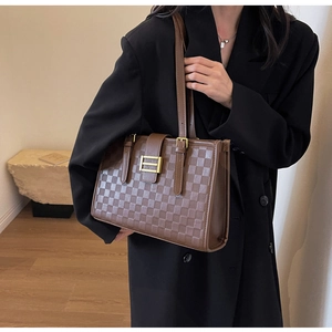 Detail of a brown checkered leather tote bag with gold buckle on a business suit model