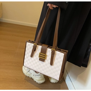 Close-up of white checkerboard tote bag with brown leather straps and gold buckle