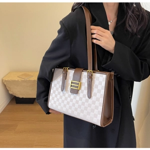 On-shoulder view of a large checkered tote bag with brown handles and gold buckle detail