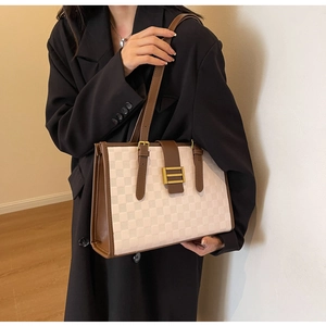 Close-up of checkered tote bag featuring brown leather trim and golden metal clasp detail