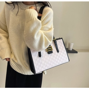 Detail of white woven tote bag featuring black trim and gold buckle worn by a model