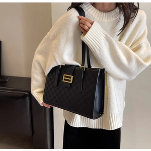 Detail of black checkered embossed tote bag with gold metal clasp on white sweater