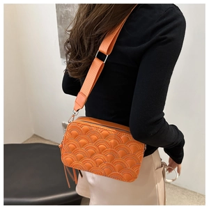 Detail of orange crossbody bag with wave quilting and wide woven shoulder strap