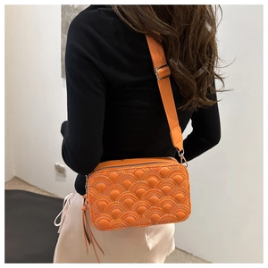 Detail of orange quilted crossbody bag with adjustable wide strap shown on model back