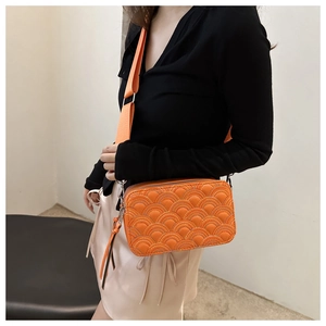 Detail of vibrant orange quilted camera bag with elegant tassel and woven shoulder strap