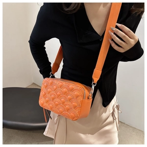 Detailed close-up of orange quilted camera bag with wide strap and silver dual zippers