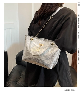 Detail of silver crocodile pattern tote bag with gold chain and H-shaped charm