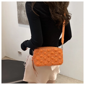 Detail of vibrant orange quilted crossbody bag with wave stitching and wide strap