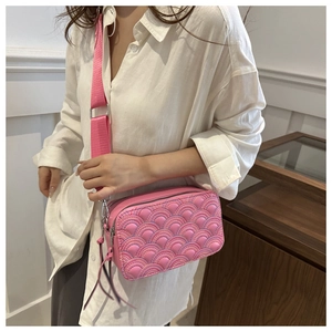 Pink quilted crossbody camera bag with wide nylon strap shown on a model outfit