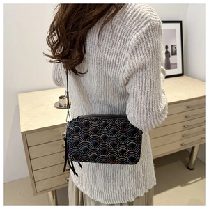 Detail of a black crossbody bag featuring rainbow quilting and studded accents on a model
