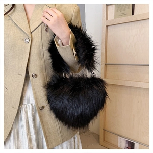 Seitenansicht einer flauschigen schwarzen Kunstfell-Herzhandtasche, präsentiert von einem Model