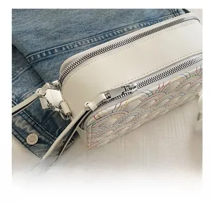 Detailed close-up of smooth silver zippers and rainbow wavy stitching on a white camera bag