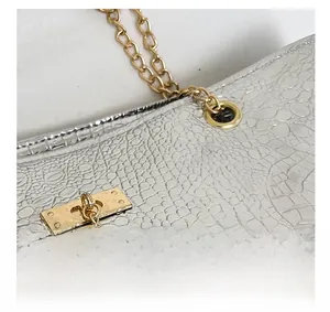 Detail of silver crocodile-embossed handbag with gold chain strap and deer pendant