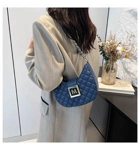 Detalle de bolso acolchado azul con hebilla logo M dorada y correa de cadena