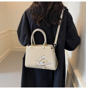 Detail of floral embroidery on a beige rectangular handbag with golden hardware