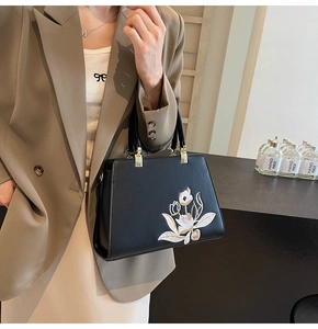 Close-up of black handbag with floral embroidery and gold hardware on model