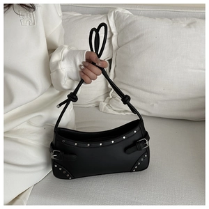 Detail of silver rivets and buckle straps on black leather shoulder bag in a clean setting