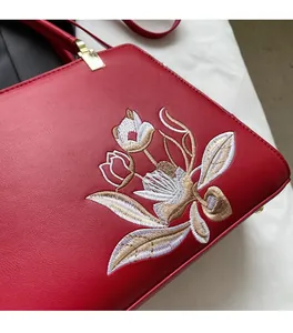 Detailed close-up of intricate gold and white floral embroidery on premium red leather bag