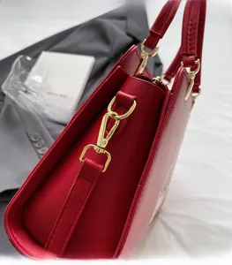 Close-up of bright red tote bag showing golden metal buckle and smooth leather texture