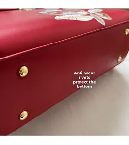 Detail of red leather bag base with golden protective studs and floral embroidery