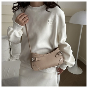 Close-up of silver studs and buckle details on a beige Y2K style crescent shoulder bag