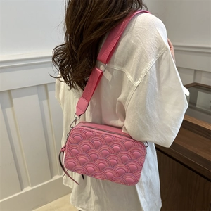 Pink quilted rainbow camera bag with wide shoulder strap worn by a model in a modern room