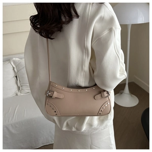 Detail of vintage beige underarm bag with silver studs worn by a model in a minimal room