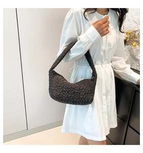 Detail of black quilted shoulder bag featuring 3D floral texture and zipper closure