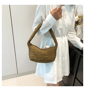 Close-up of brown quilted shoulder bag with floral stitching and padded texture on model