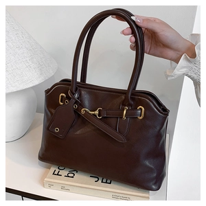 Détail du cabas en cuir marron foncé avec mors doré et longues anses pour un look chic