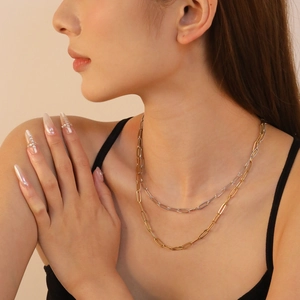 Détail de colliers trombones superposés en or et argent portés par un mannequin en noir