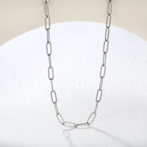 Vue verticale du collier chaîne trombone en argent poli sur un support minimaliste beige