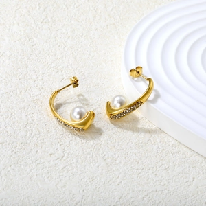 Gold C-shape earrings with pearls and small diamonds on white stone background