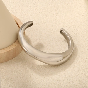 Irregular C-shaped silver open bangle with polished mirror finish on a minimalist wooden stand