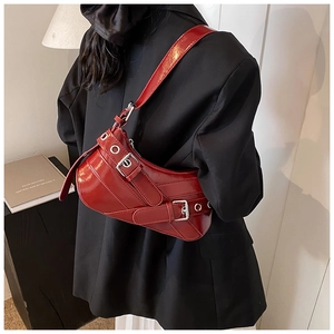 Détail du sac à épaule en cuir verni rouge avec œillets sur un blazer noir