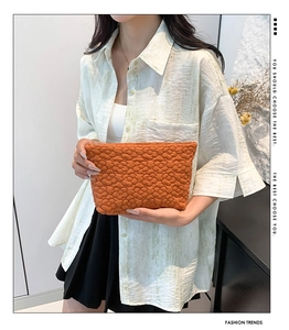Detail of orange quilted envelope clutch with floral stitching and padded texture
