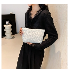 Detail of white clutch with 3D floral texture held by a model in a black cardigan